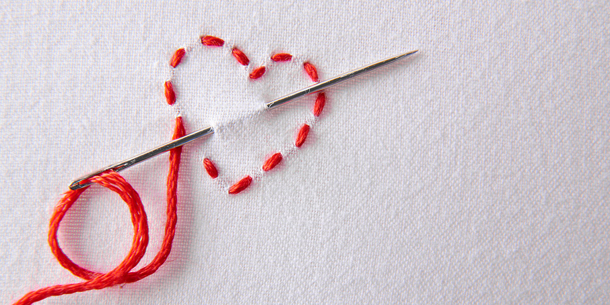 Needle with thread sewing a heart into fabric